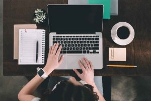 Rugalmas diákmunkát végző fiatal egy irodában laptoppal, jegyzetfüzettel, kávéval