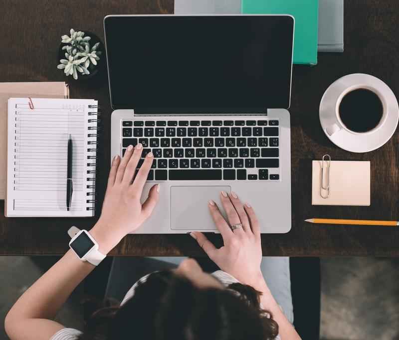 Rugalmas diákmunkát végző fiatal egy irodában laptoppal, jegyzetfüzettel, kávéval