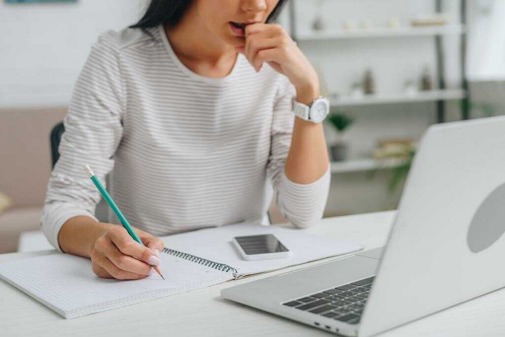 Fiatal lány a munka és tanulás összeegyeztetése közben egy laptop és jegyzetfüzet előtt